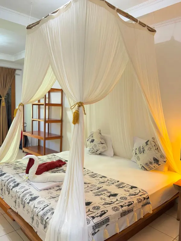 Un lit à baldaquin drapé de voilages blancs se trouve dans une chambre lumineuse.