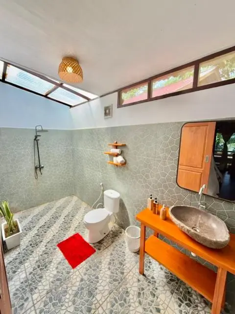 Salle de bain ouverte avec douche à l'italienne et lavabo en pierre.
