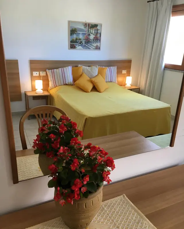 Une chambre lumineuse avec un grand lit recouvert d'une couverture jaune et de coussins colorés.