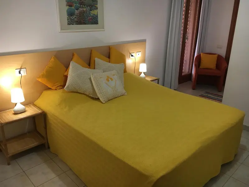 Une chambre lumineuse avec un grand lit recouvert d'une couverture jaune et de coussins colorés.