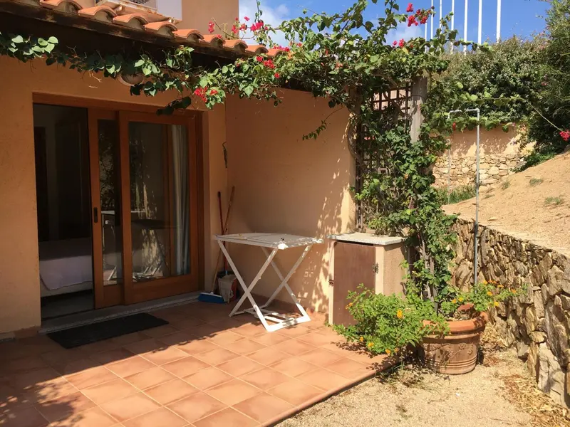 Terrasse ombragée avec table et chaises devant une porte-fenêtre.