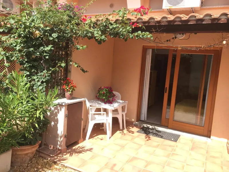 Une petite terrasse ombragée avec une table et des chaises devant une porte-fenêtre.