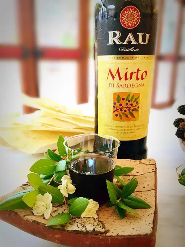 Une bouteille de liqueur et un verre sur une planche en bois décorée de feuilles et de fleurs.