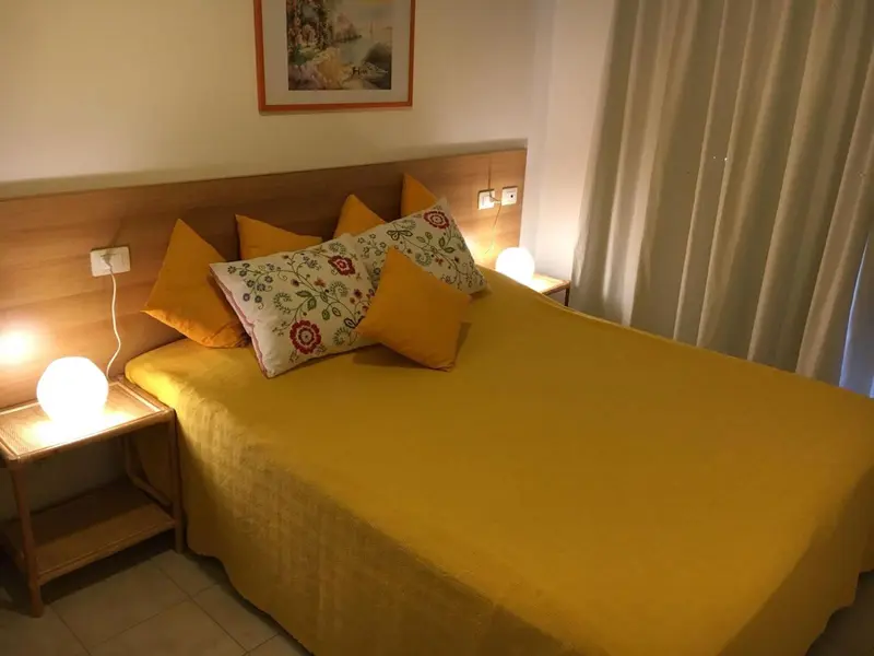Lit jaune avec coussins fleuris dans une chambre lumineuse.