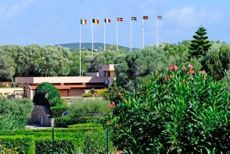 Bâtiment bas entouré de végétation luxuriante et de drapeaux flottant au vent.