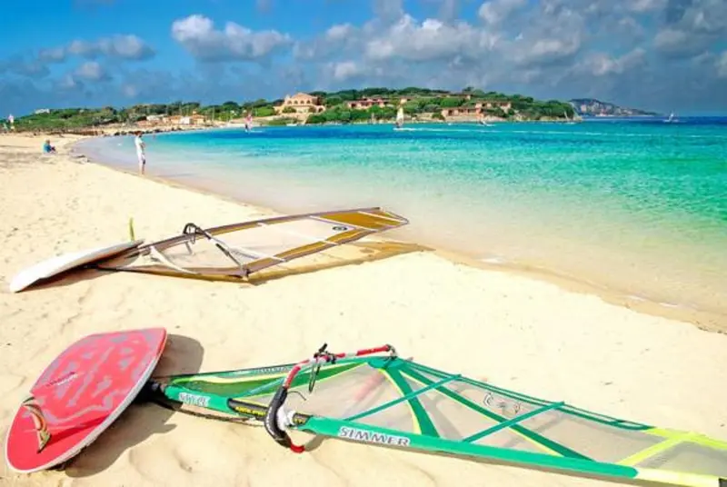 Planche de windsurf posée sur une plage de sable blanc bordée d'eau turquoise.