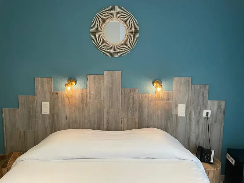 Un lit blanc est dispose devant une tete de lit en bois decorative et un mur bleu turquoise.