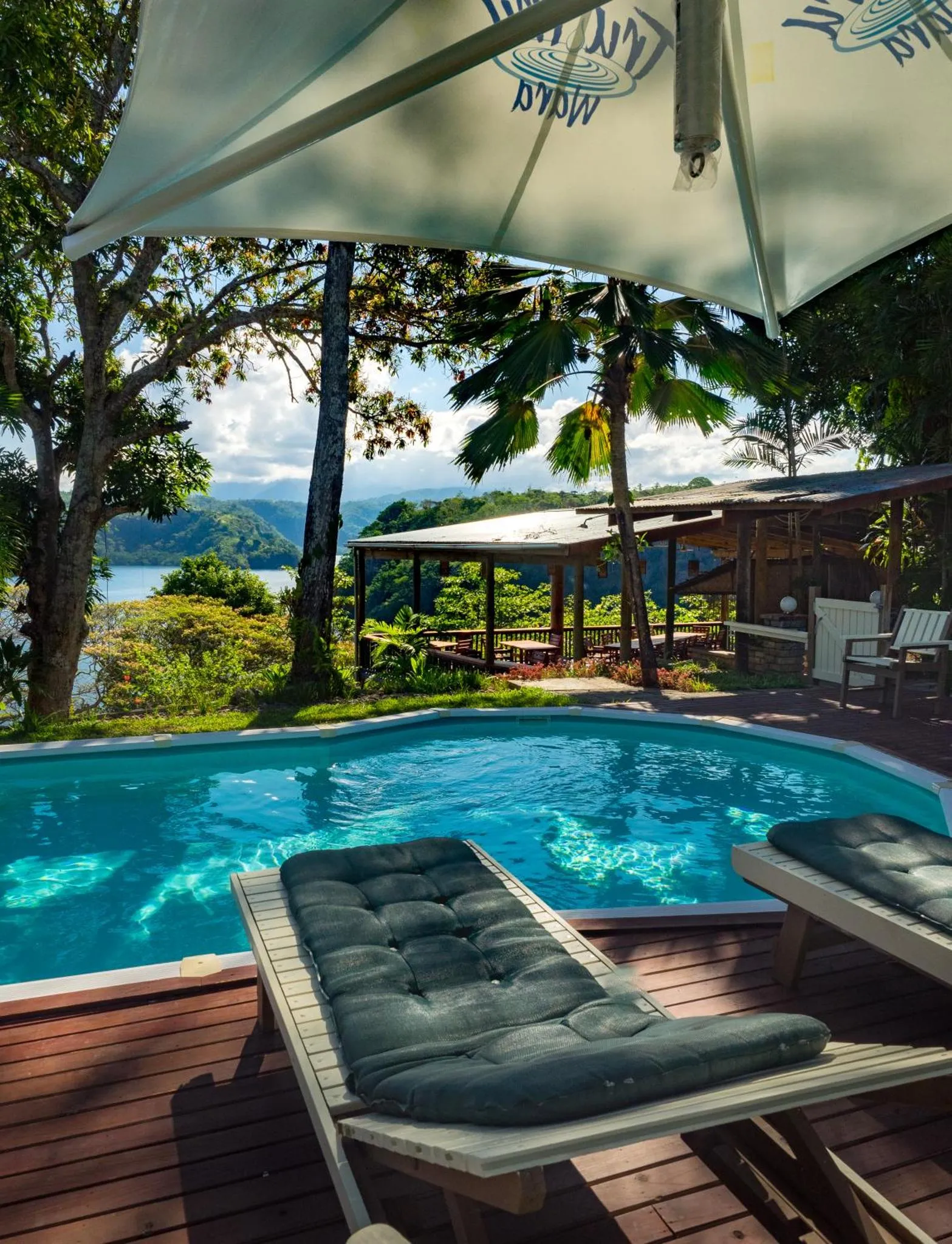 Transats bleus au bord d'une piscine turquoise avec vue sur la mer et la végétation.