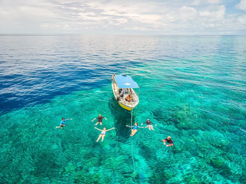 Vue aérienne d'un bateau de plaisance et de personnes flottant dans une eau turquoise.