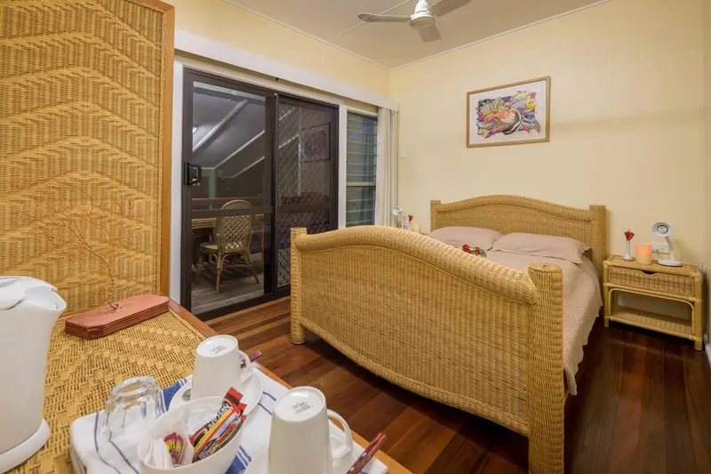 Chambre lumineuse avec un lit en rotin et une terrasse accessible par une baie vitrée.