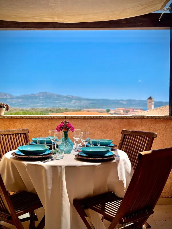 Une table dressée sur une terrasse offre une vue sur la mer et les montagnes.