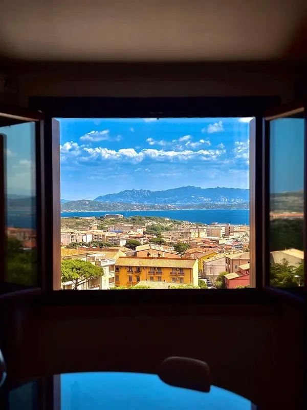 Vue sur une ville côtière et les montagnes depuis une fenêtre.