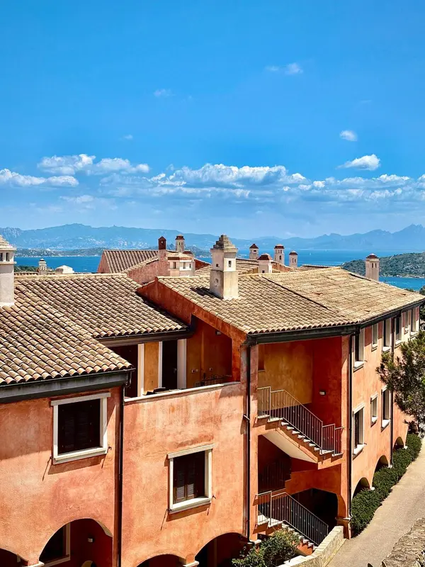 Vue d'ensemble d'un complexe immobilier aux toits de tuiles rouges et aux murs ocres, avec une vue sur la mer et les montagnes.