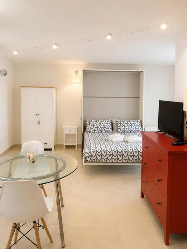Une chambre lumineuse avec un lit fait et un coin repas.