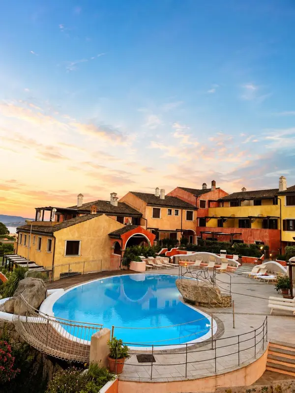 Vue d'un complexe hôtelier avec une piscine au premier plan et un coucher de soleil en arrière-plan.