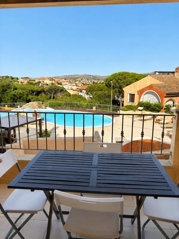 Une table et des chaises blanches sont disposées sur une terrasse avec vue sur une piscine et un paysage verdoyant.
