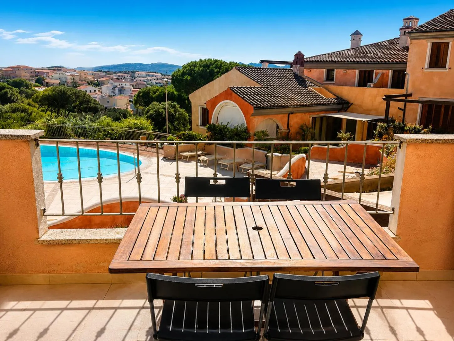 Terrasse avec table et chaises donnant sur une piscine et un paysage urbain.