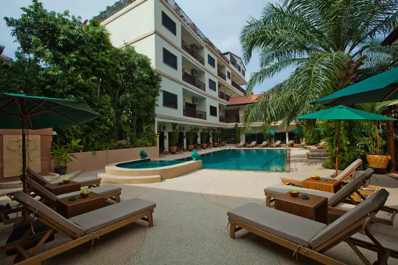 Transats et parasols bordent une piscine dans un jardin tropical.