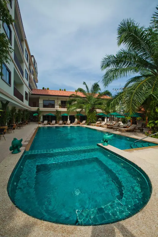 Une piscine rectangulaire turquoise avec un jacuzzi intégré, entourée de chaises longues et de végétation tropicale.