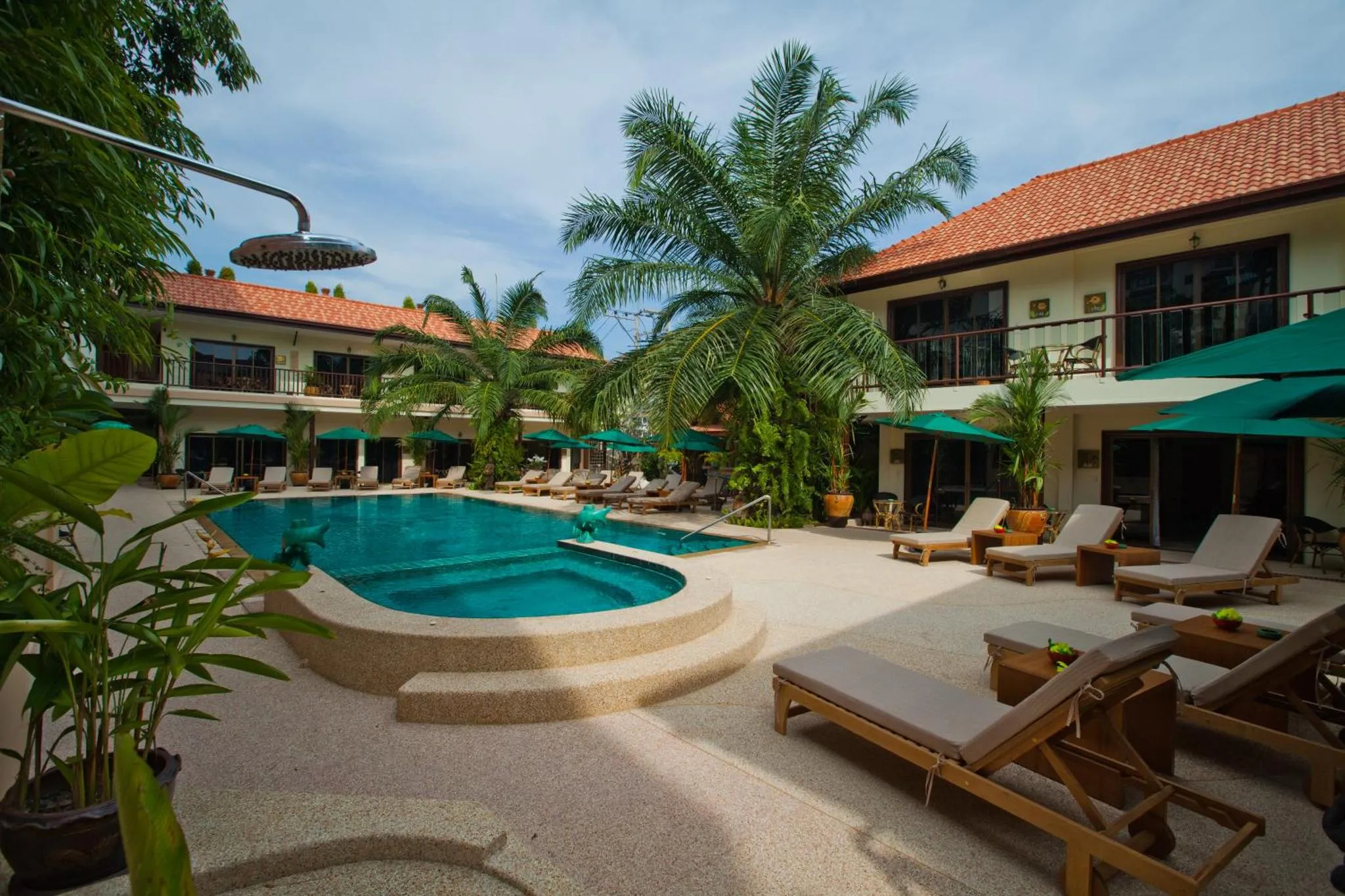 Une piscine bordée de transats et de végétation tropicale devant un bâtiment à l'architecture soignée.