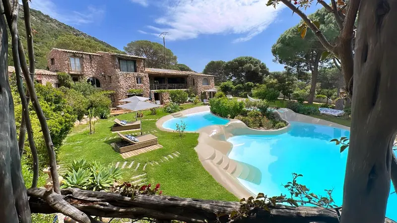 Bâtiment en pierre avec piscine et végétation luxuriante.