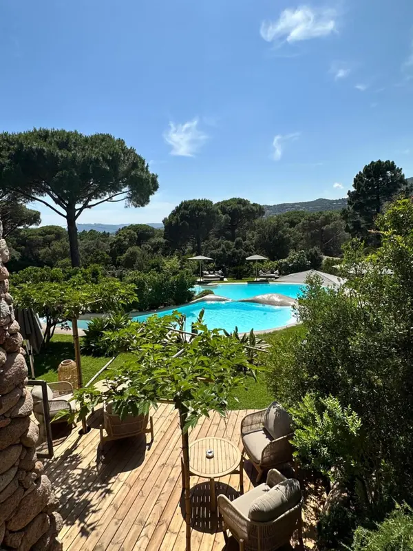 Terrasse en bois avec mobilier de jardin donnant sur une piscine et un paysage verdoyant.