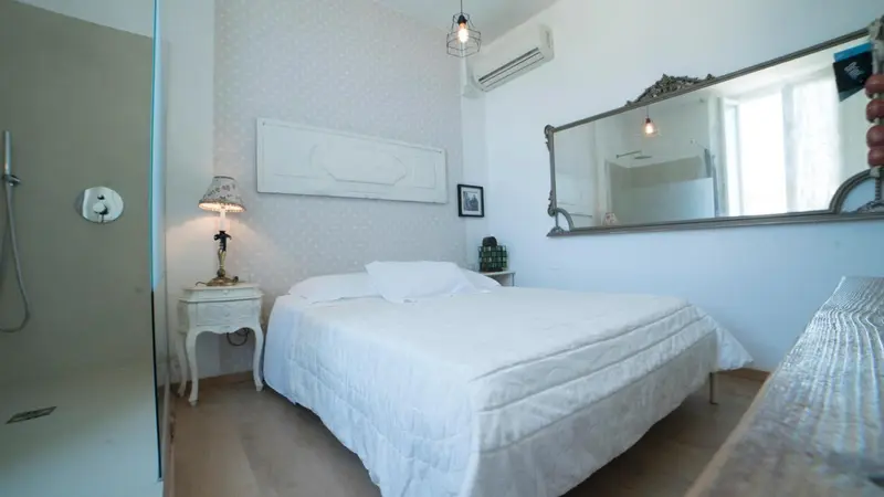 Une chambre lumineuse avec un lit blanc et un grand miroir.