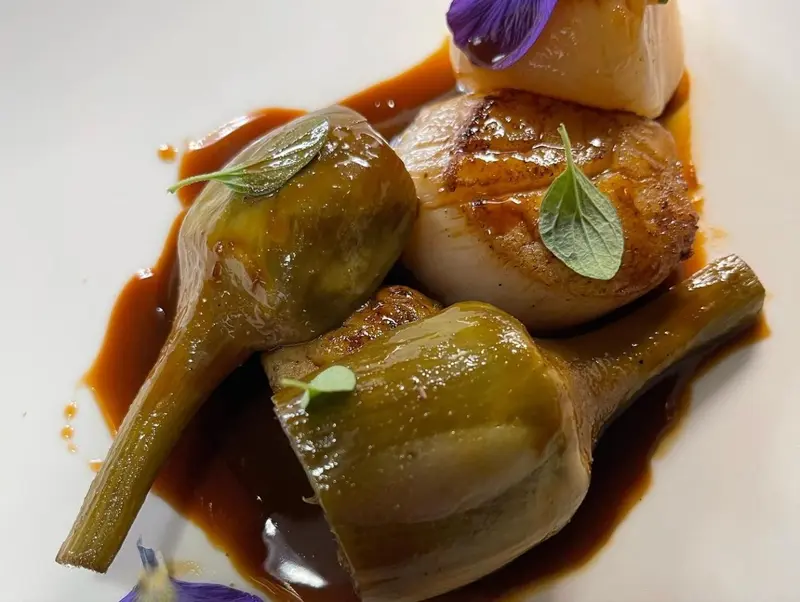 Assiette de coquilles Saint-Jacques et d'artichauts violets nappés d'une sauce brune.