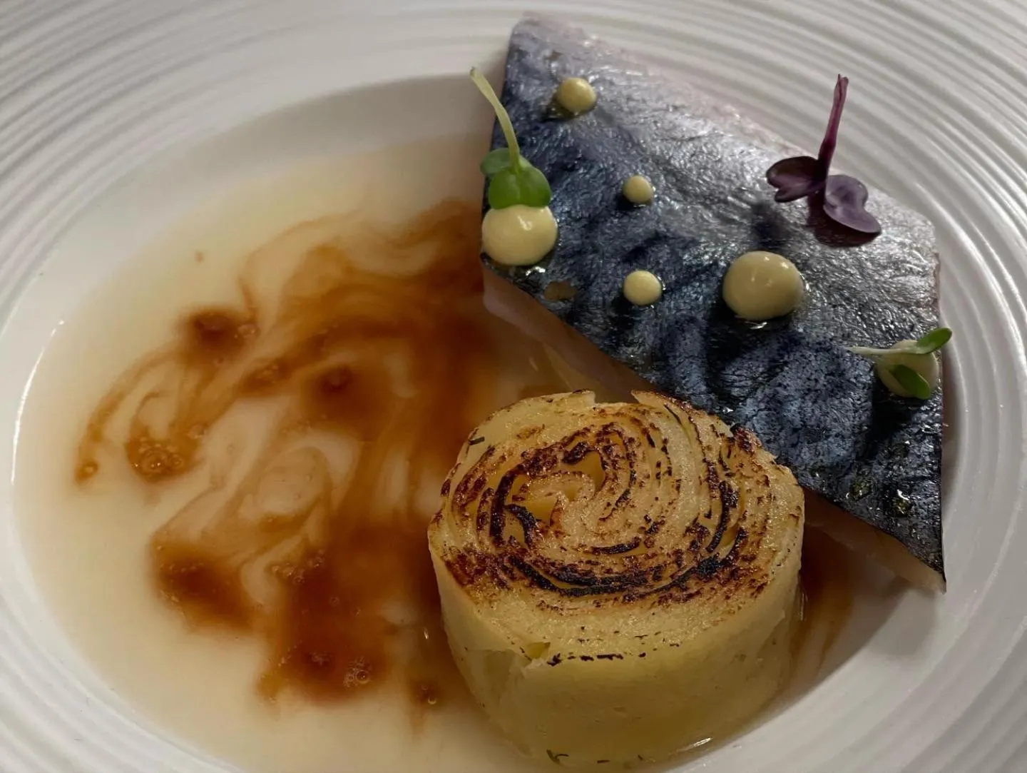 Assiette gastronomique avec un poisson, une sauce et des légumes.