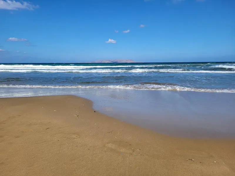 Une plage de sable fin borde une mer turquoise sous un ciel bleu clair.