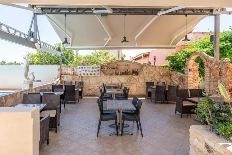 Terrasse ombragée avec tables et chaises en osier.