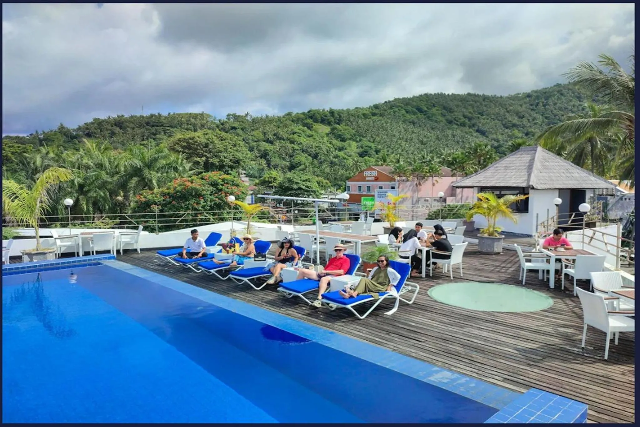 Des transats bleus bordent une piscine turquoise sur une terrasse ensoleillée.