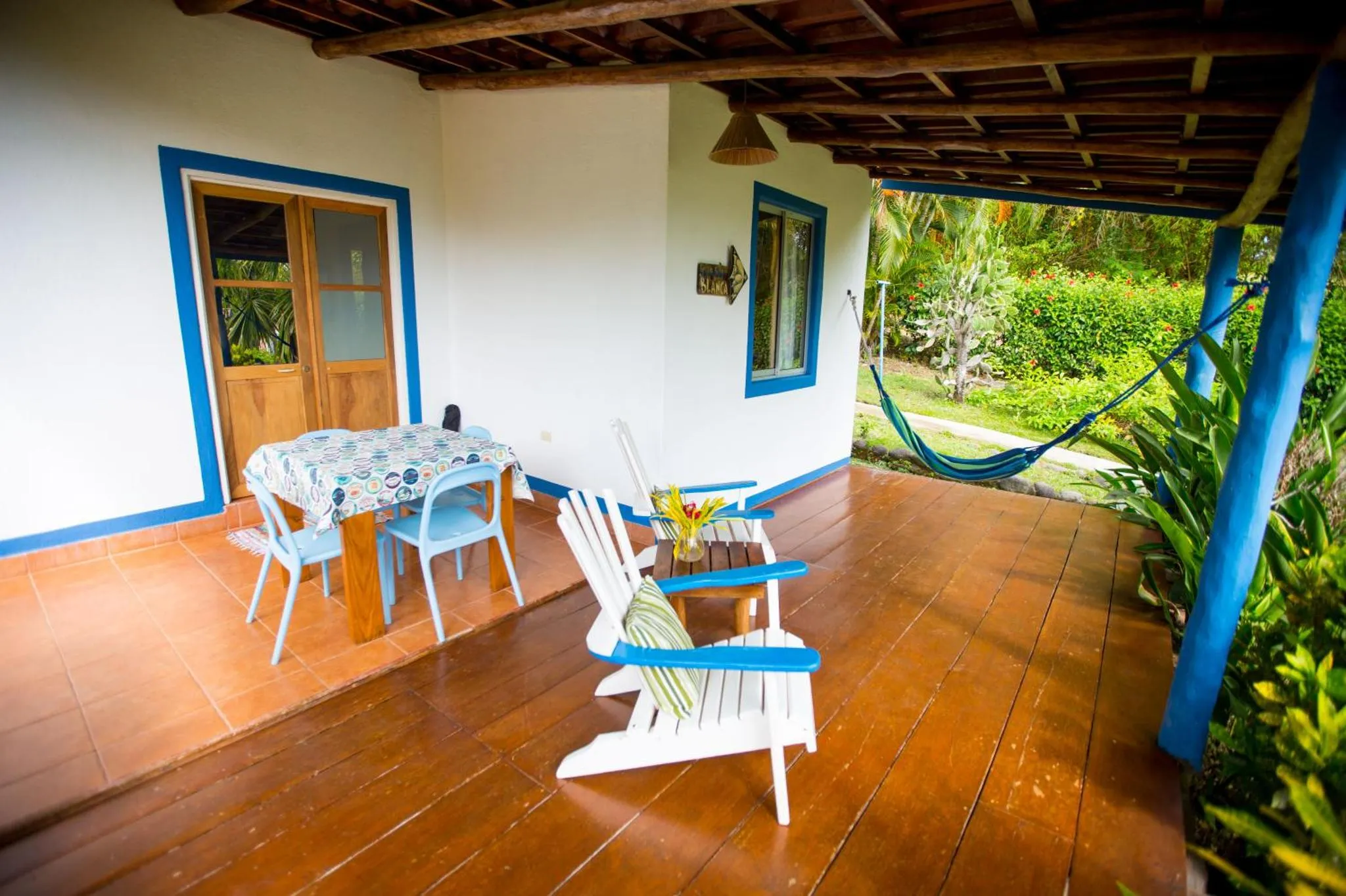 Terrasse ombragée avec table et chaises en bois, agrémentée de fauteuils et d'un hamac.