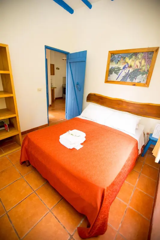 Une chambre lumineuse avec un lit recouvert d'une couverture orange et un tableau au mur.