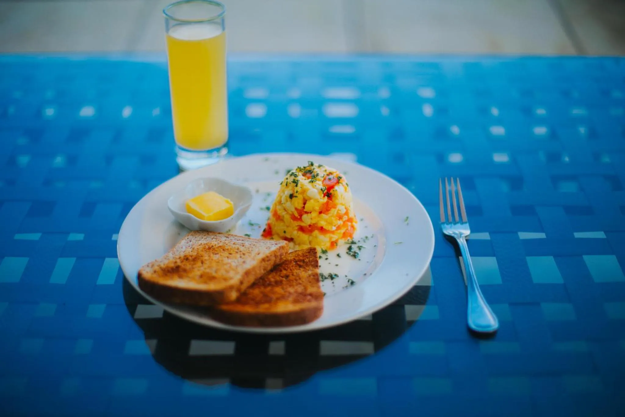 Un petit-déjeuner avec des œufs brouillés, du pain grillé et un jus d'orange est présenté sur une table.