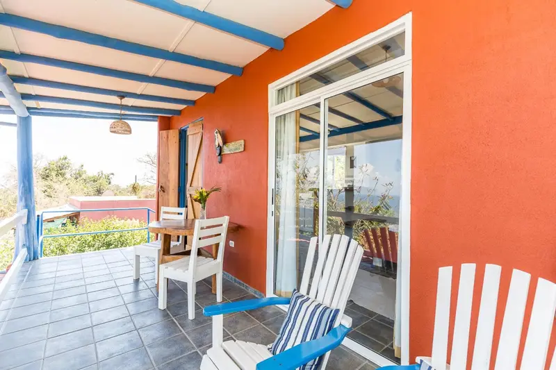 Terrasse carrelée avec mobilier blanc et rouge, donnant sur un espace extérieur.