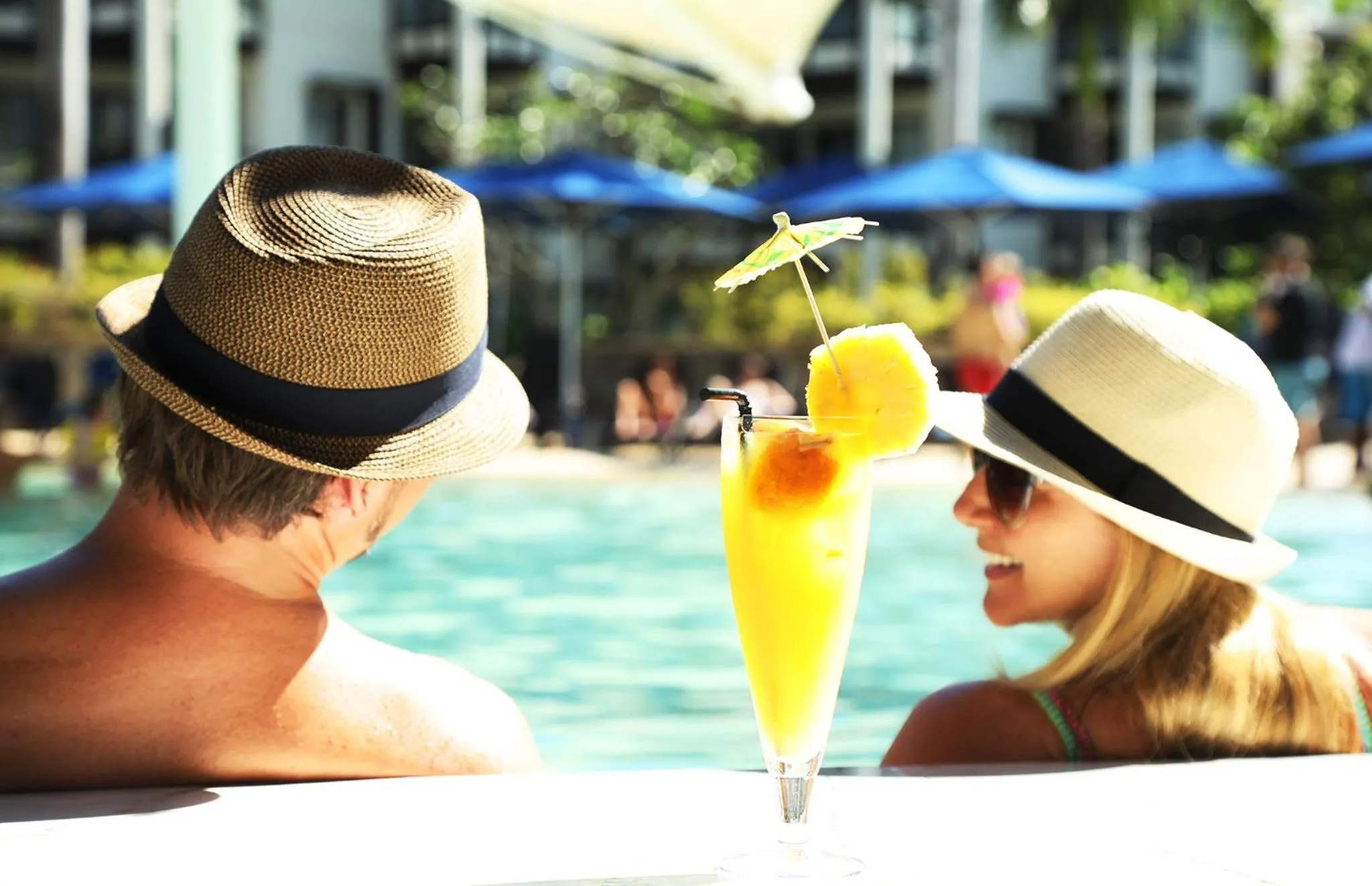 Deux personnes en chapeau savourent des boissons au bord d'une piscine.