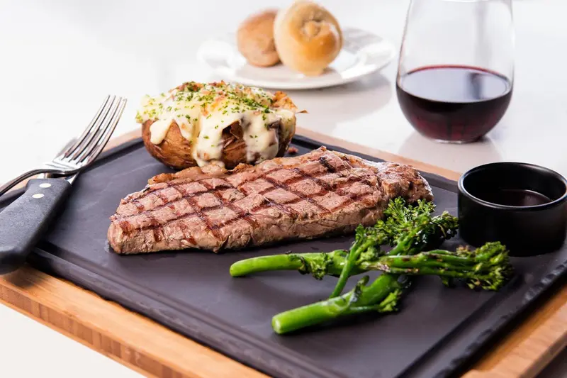 Un plat de viande grillée accompagné de légumes et de pain est présenté sur une planche.