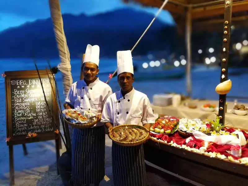 Des cuisiniers présentent des plats de fruits de mer sur une plage ensoleillée.