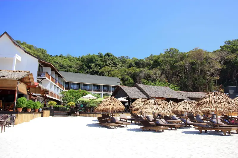 Transats et parasols de plage devant un bâtiment blanc et une végétation luxuriante.