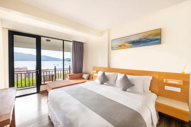 Chambre lumineuse avec un grand lit et un accès à une terrasse offrant une vue sur la mer.