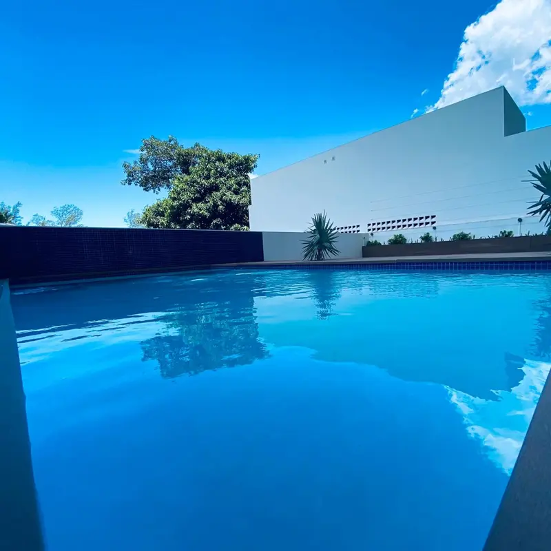 Une piscine rectangulaire turquoise reflète le ciel bleu et les nuages.
