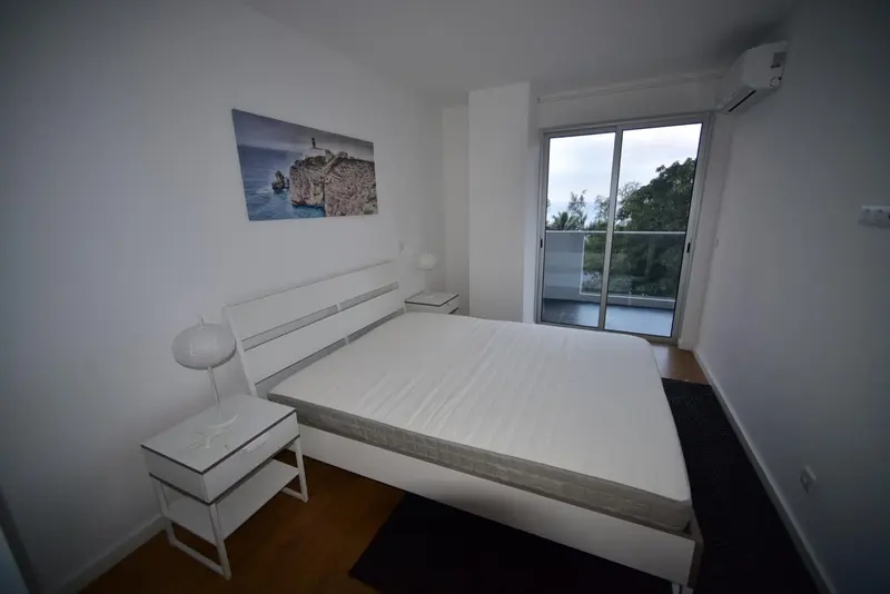 Chambre lumineuse avec un grand lit blanc et un accès à une terrasse.