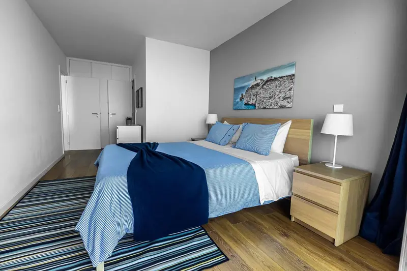 Une chambre lumineuse avec un grand lit recouvert d'une couverture bleue et de coussins.