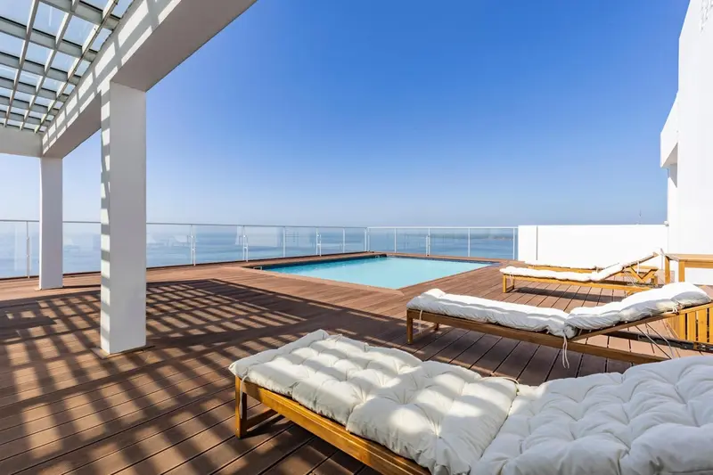 Terrasse avec transats et piscine au bord d'une vue sur la mer.
