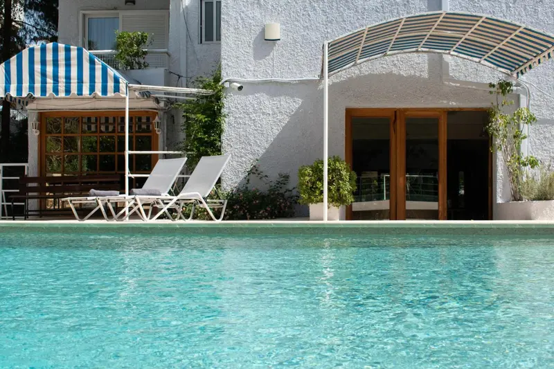 Deux transats blancs sont placés devant une piscine turquoise, sous un auvent rayé bleu et blanc.