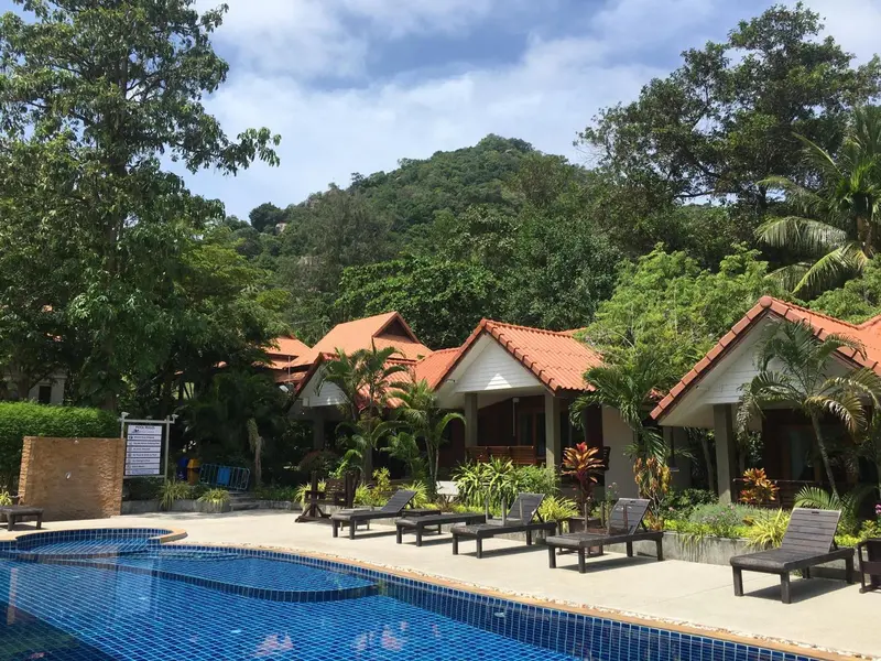 Des bungalows aux toits rouges bordent une piscine turquoise dans un cadre tropical.