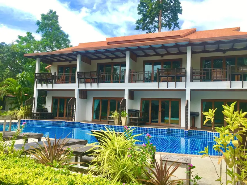 Bâtiment blanc à deux étages avec des balcons et une piscine au premier plan.