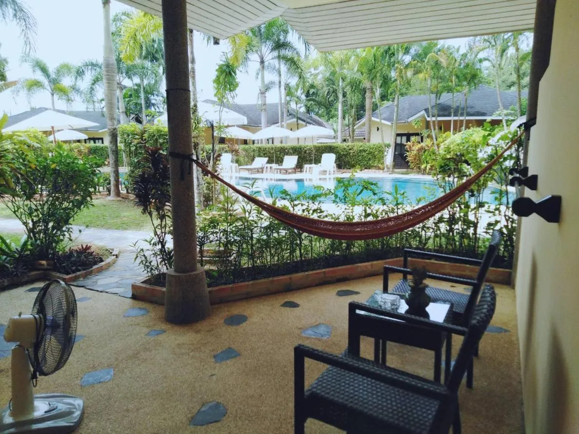 Un hamac est suspendu sur une terrasse avec des meubles de jardin et une piscine en arrière-plan.