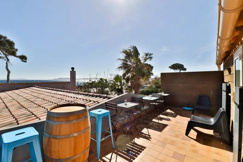 Terrasse avec tables et chaises offrant une vue sur la mer et la végétation.